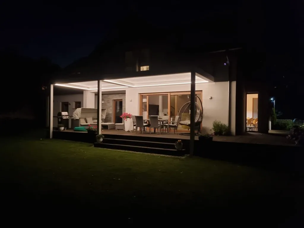 An aluminium pergola over a terrace with LED lighting along the roof outline, at night
