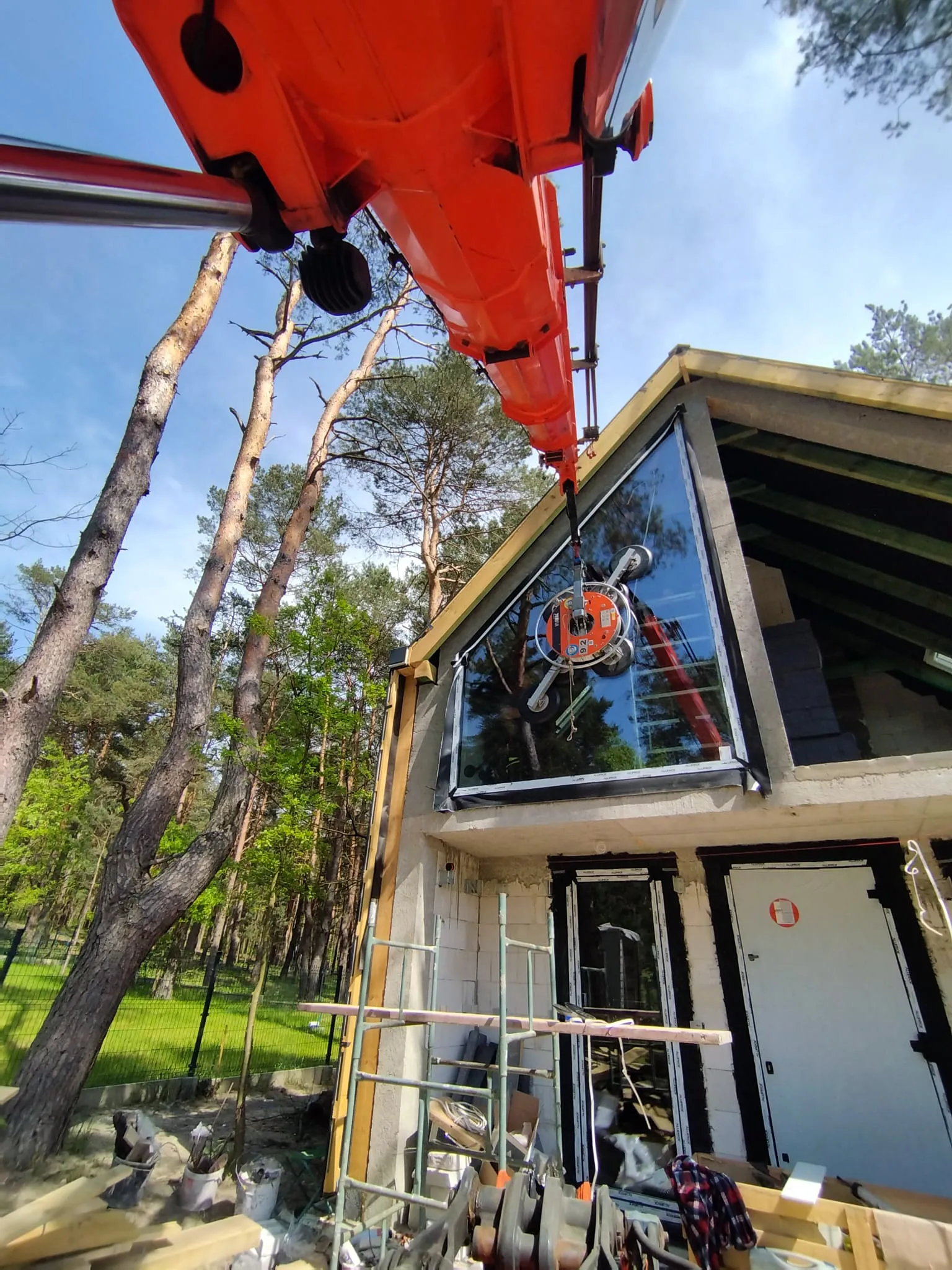 Crane installing a large-format triangular glazing unit at a house build in the forest